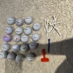 Golfbollar och peggar  - Bilden visar ett set med golfbollar från olika märken samt flera peggar och ett orange verktyg. Perfekt för dig som vill komma igång med golf eller behöver extra bollar och peggar till nästa runda. Passar både nybörjare och erfarna golfare.
