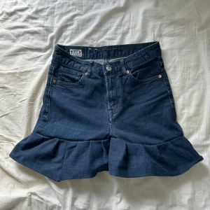 Mörkblå volangkjol från KOI - Unik mörkblå jeans kjol från KOI med volang nertill. Klassisk femficksmodell, knapp- och dragkedjestängning samt bälteshällor. Snygg midja och cool volangdetalj som ger en extra edge till din sommarstil. Sytt själv. Buda gärna 😇😇