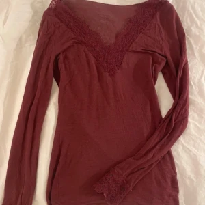 Vinröd intimissimi långärmad topp med spets - Vinröd långärmad topp med snygg v-ringning och spetsdetaljer både vid halsen och ärmsluten. Tunn och mjuk, perfekt att styla med jeans eller kjol. Figurnära passform och enkel att bära till olika looks.