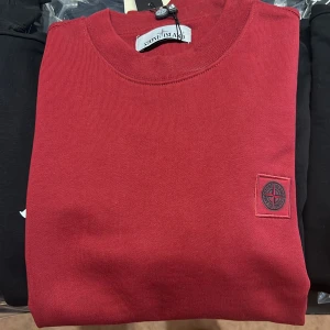 Röd sweatshirt från Stone Island - Snygg röd sweatshirt från Stone Island med klassisk rund hals och ikonisk kompasslogga på bröstet. Tröjan är i mjuk bomull och har långa ärmar. Perfekt för dig som gillar stilrena och trendiga plagg med streetkänsla. Finns i alla storlekar 