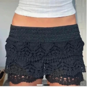 Svarta virkade shorts med spetsdetaljer -  STORLEK XS/S.                         Snygga svarta shorts med bred resår i midjan och vackra virkade spetsdetaljer i lager på lager. De har en feminin look med vågig kant nertill och är perfekta för varma dagar. Superbekväma och lätta att matcha med en enkel topp.