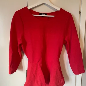 Röd tröja från Bik Bok - Snygg röd tröja från Bik Bok med trekvartsärm och omlottdetalj i ryggen. Klänningen har en markerad midja och är tillverkad i ett strukturerat, stretchigt material som sitter bekvämt. Perfekt för dig som vill sticka ut med en enkel men cool look. Använd 1 gång 
