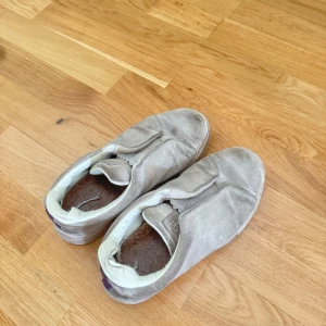 Eytys sneakers mocka - Stilrena slip-on sneakers från Eytys i grå mocka med vit sula och diskreta detaljer. Skorna har rund tå och elastiska partier på ovansidan för enkel påtagning. Perfekta för dig som gillar en clean och enkel look.