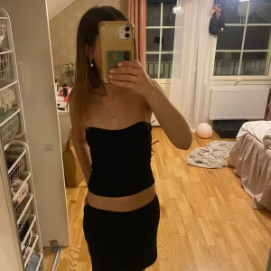 Svart ribbad tubtopp Gina Tricot XS - Säljer en svart ribbad tubtopp från Gina Tricot i storlek XS. Toppen är bandeau-modell, axelbandslös och har en snygg struktur med markerade sömmar framtill. Perfekt att styla med kjol eller jeans för en clean look.