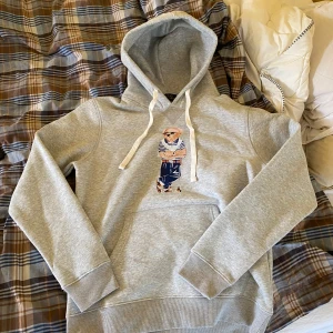 Grå Polo Ralph Lauren Polo Bear hoodie - Snygg grå hoodie från Polo Ralph Lauren med ikoniska Polo Bear-trycket framtill. Otroligt trendig och stilren tröja. Skicket är topp och nästan aldirg använd. Säljer pga att den är för liten för mig. Hör av dig vid fler frågor eller funderingar!😁☀️