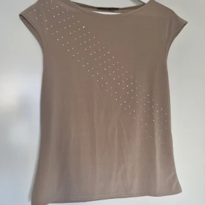 Gammelrosa topp med små glittriga stenar H&M - Topp från H&M med glittrande stenar diagonalt över framsidan. Mjuk och stretchig i polyester.