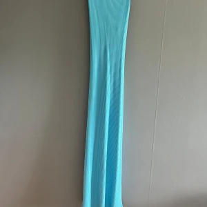 Lång ribbad blå klänning med korsrygg - Supersnygg långklänning i ribbad blått tyg från H&M. Klänningen har breda axelband som korsas i ryggen och en tight passform som framhäver figuren. Perfekt för dig som vill sticka ut med en cool och fräsch look i sommar.