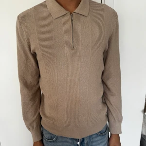 Beige stickad polotröja med half zip - Snygg beige stickad polotröja med krage och half zip-dragkedja framtill. Tröjan har långärmad passform och diskret ribbade detaljer på framsidan. Perfekt för dig som gillar en clean och stilren look.