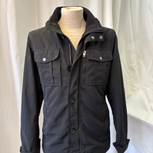 J.Lindeberg field jacket - Stilren svart fieldjacka från J.Lindeberg i en snygg och eftertraktad modell. Jackan passar bra till regn, vind och även kallare väder.