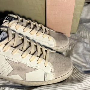 Golden Goose sneakers med leoparddetalj - Snygga Golden Goose sneakers i vitt skinn med beige mockadetaljer och ikonisk stjärna på sidan. Hälpartiet har coolt leopardmönster som ger extra edge. Klassisk snörning och svartvit GGDB-logga på plösen. Perfekta för dig som vill sticka ut med stil. Perfekt för dig som vill ha en unik look. OBS lnte 0rglnal 