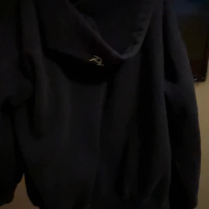 Mörkblå fleecejacka med dragkedja - Mysig mörkblå fleecejacka med dragkedja framtill och broderad text på bröstet. Jackan har en avslappnad passform och är perfekt för kyliga dagar. Stilen är enkel och passar till det mesta, med mjukt material som känns skönt mot huden.