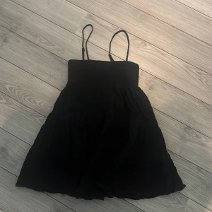 Svart kort klänning från Zara XS - Supersöt svart kort klänning från Zara med smockad överdel och tunna axelband. Kjolen är lätt utställd och tyget känns luftigt, perfekt för varma dagar. Enkel och stilren design som är lätt att matcha med accessoarer.