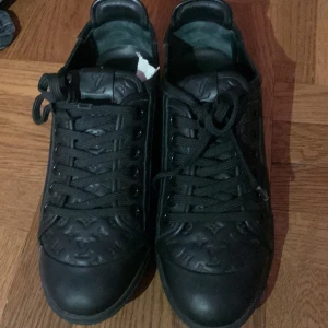 Svarta Louis Vuitton sneakers i skinn - Snygga svarta Louis Vuitton sneakers i skinn med klassiskt LV-monogram präglat på tån och plösen. Skorna har rund tå, platt sula och svarta snören. Kommer med original dustbag. Perfekta för dig som gillar exklusiva detaljer och stilren design.