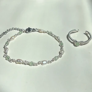 New Jade Set - Setet innehåller: ✓ Ett handgjort armband ✓ En justerbar ring  Armband: Längd: 16,5 cm + 6,5 cm förlängningskedja Material: Rostfritt stål, äkta sötvattenspärlor och New Jade (ädelsten)  Ring: Justerbar storlek Material: Rostfritt stål med äkta New Jade (ädelsten)