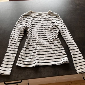 Randig långärmad tröja Gina Tricot - Snygg långärmad tröja från Gina Tricot i vitt med svarta horisontella ränder. Modellen är figurnära med rund halsringning och tillverkad i mjuk bomull. Perfekt för en enkel och stilren look.