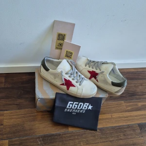 Golden Goose vita sneakers med röd stjärna  - Golden Goose sneakers i vitt skinn med ikonisk röd stjärna på sidan, grå snörning och grågrön häl med logga. Allt på bilden ingår för endast 1499 kr. Skriv om ni har fler frågor!