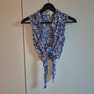 Knytblus x Whitney Port - Supersöt blommig blus i blått och vitt från Whitney Port x Bik Bok. Ärmlös modell med krage och långa band framtill som kan knytas i midjan. Vita knappar. Perfekt för en chill sommarlook och till jeans eller kjol. Materialet är mjukt och svalt i viskos.