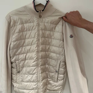 Äkta Cardigen jacka från Moncler - Snygg beige Cardigen jacka från Moncler med ribbad krage och ärmar. Jackan har dragkedja framtill, två fickor med tryckknappar och Moncler-logga på ärmen. Materialmix med polyester och bomull ger en stilren look. Det finns äktighetsbevis vid intresse så de bara att höra av sig!!