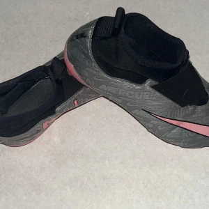 Grå och rosa fotbollsskor från Nike - Snygga grå fotbollsskor från Nike med rosa detaljer och en stilren design. Skorna har en elastisk passform och är perfekta för snabba rörelser på planen.