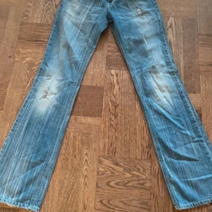 Blå jeans med slitningar - Säljer ett par svin snygga blå jeans med coola slitningar och en klassisk femficksdesign. De har en lågmidjad design och är tillverkade i denim.