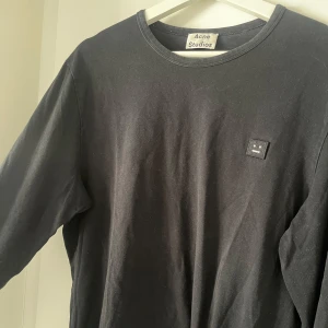 Svart långärmad tröja från Acne Studios - Säljer en stilren svart långärmad tröja från Acne Studios. Tröjan har en liten logotyp på bröstet och är tillverkad i mjuk bomull. Perfekt för en avslappnad look. Nypris: 1499kr