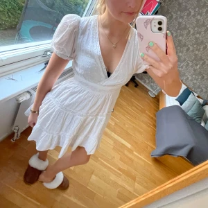 Vit kortklänning med puffärmar - Säljer en söt vit kortklänning med puffärmar och v-ringning. Klänningen har fina spetsdetaljer och en omlott-design. Perfekt för sommaren och skolavslutning! Den är använt sparsamt🥰