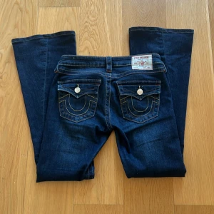 Mörkblå jeans från True Religion strl 26 - Snygga mörkblå jeans från True Religion med bootcut-stil. De har dekorativa bakfickor med knappar och kontrastsömmar. Perfekta för en avslappnad look. Är i jättebra skick, använda ett fåtal ggr. 