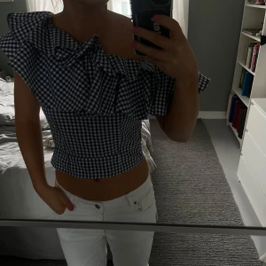 Blårutig offshoulder topp - Säljer en snygg blårutig offshoulder topp med volangdetaljer. Har dragkedja vid sidan av magen. Kan både bäras off shoulder och bara på ena axeln. 