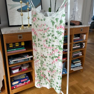 Blommigt nattlinne - Säljer ett sött blommigt nattlinne från Lindex med gröna och rosa blommor på vit bakgrund. Klänningen har smala axelband och spetsdetaljer vid halsringningen. Mjuk och andningsbar viskos. Perfekt för en somrig look!