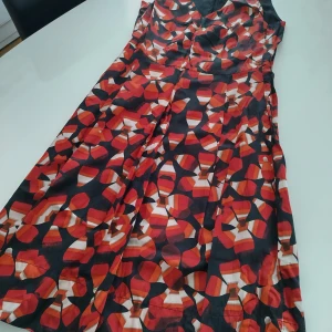 Mönstrad klänning från Turnover - Snygg klänning från Turnover med ett färgstarkt mönster i rött, svart och vitt. Klänningen har en v-ringad design och är ärmlös, vilket gör den perfekt för varmare dagar. Tillverkad i en blandning av siden och bomull för en lyxig känsla.