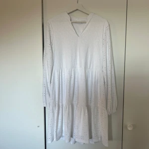 Vit långärmad klänning  - Säljer en vit långärmad klänning från vila med v-ringning och volangdetaljer. Klänningen har ett diskret broderat mönster och är perfekt för vår och sommar. Den är både stilren och bekväm. Passar perfekt till sommaren och även studenten🤍