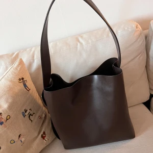 Brun skinn tote (som ny från Arket)  - Brun tote/väska i 100% skin, köpt från Arket och använd ca 3 gånger. Perfekt för jobb/skola då dator och liknande får plats. Väskan har en bred justerbar axelrem och en innerficka med dragkedja ✨Nypris 3290 kr. Länk: https://www.arket.com/sv-se/product/tote-bag-dark-brown-1173813005/