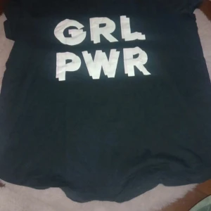 Svart t-shirt med texten GRL PWR - Snygg svart t-shirt med det kraftfulla budskapet 'GRL PWR' i vit text på framsidan. Perfekt för att visa upp girl power! Kortärmad och bekväm passform.