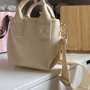 Beige axelväska från H&M - Säljer en stilren beige axelväska från H&M. Väskan har en avtagbar axelrem med guldfärgade detaljer och är tillverkad i ett slitstarkt material. Perfekt nu inför sommar💕