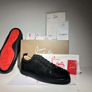  Christian Louboutin skor - Snygga svarta sneakers från Christian Louboutin med nitar på tåpartiet. Skorna har en klassisk snörning och den ikoniska röda sulan. Perfekta för att ge en edgy touch till din stil.