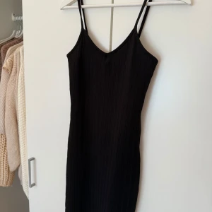Svart ribbad klänning - Snygg svart ribbad klänning med smala axelband och v-ringning. Perfekt för en stilren look.