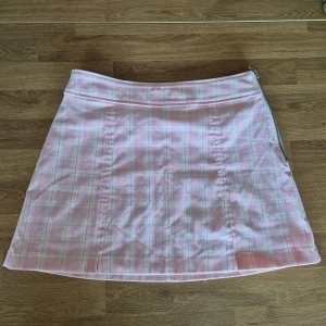 Rutig rosa kjol från Pimkie - Säljer en söt rosa rutig kjol från Pimkie med dragkedja på sidan. Kjolen har en kort längd och är perfekt för en trendig look. Den har en stilren design med en lätt A-linjeform. Storleken är uppskattad då märkning saknas.