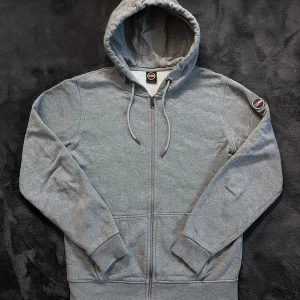 Colmar zip hoodie - Säljer en stilren grå hoodie från Colmar med dragkedja och huva. Perfekt nu för våren. Den har en broderad logga på ärmen och mjukt foder inuti. Köpt på Zalando, storlek L, skick 8/10 är använd. Pris går att diskutera ✅