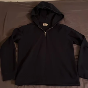 Mörkblå half zip hoodie från East West - Säljer en stilren mörkblå hoodie från East West med dragkedja framtill. Perfekt för en avslappnad look. Väldigt bra skick, inga defekter. Storlek M.