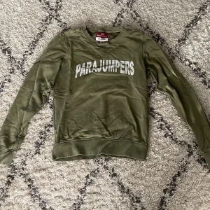Parajumpers Grön tröja  - Säljer en grön fleece tröja från Parajumpers med tryck på framsidan och ett märke på ärmen. Tröjan har långa ärmar och ribbade muddar vid ärmslut och nederkant. Perfekt för kyliga dagar!