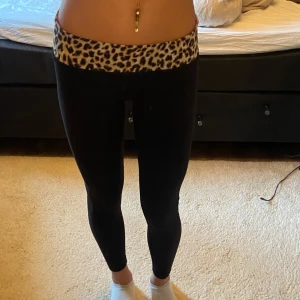 lågmidjade träningsbyxor ifrån PINK - Snygga svarta leggings med en bred leopardmönstrad midja som kan vikas ner för att istället göras rosa. Detta leggings är super gamla och går ej att få tag i längre. Från PINK ”victora’s secret”. Lågmidjadjade från första början, men ännu mer lågmidjade när kanten viks ned. Jag har vanligtvis storlek xs eller 34 i byxor och dessa sitter helt perfekt på mig. För referens är jah 170cm lång ❤️❤️Använda väldigt varsamt, så finns inga skador på tightsen 