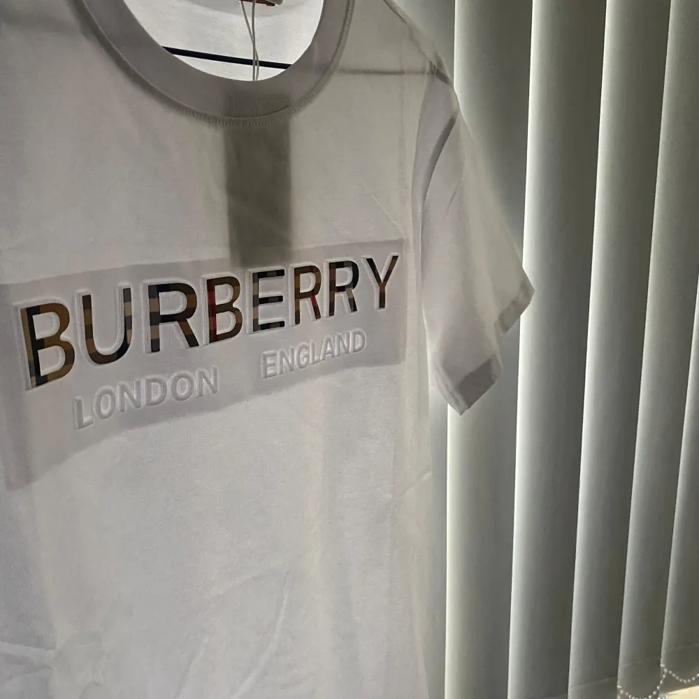 Snygg vit t-shirt från Brbery med deras ikoniska logga i relief på bröstet. Texten 'London England' är också tryckt under loggan. Perfekt för en stilren och klassisk look.. T-paidat.