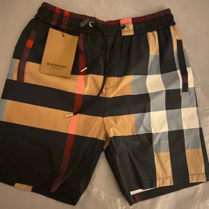  Burberry shorts - Snygga shorts från Burberry med klassiskt rutigt mönster i svart, beige, röd och vit. De har en elastisk midja med snörning för extra komfort. Perfekta för en stilren look. Säljer då den var för liten storlek för mig.