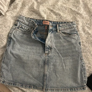 Jeanskjol från ONLY - Snygg jeanskjol från ONLY i klassisk blå denim. Kjolen har en kort längd med femficksdesign och knappgylf. Perfekt för en avslappnad stil.