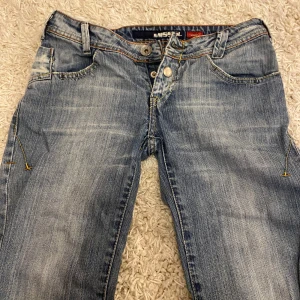 Blå low waist jeans från Miss Sixty - Snygga blå jeans från Miss Sixty med en klassisk femficksdesign och slitna detaljer. De har en låg midja och en bootcut-stil som ger en avslappnad look. Perfekta för en casual outfit!