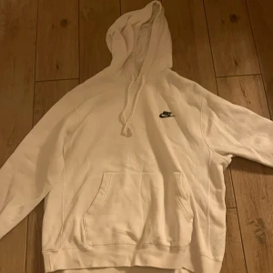 Vit hoodie från Nike - Säljer en stilren vit hoodie från Nike med klassisk logga på bröstet. Den har en rymlig ficka framtill och justerbar huva med dragsko. Perfekt för en avslappnad look.
