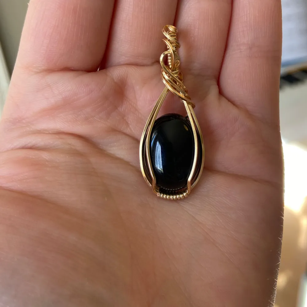 Elegant hänge med en stor svart sten infattad i en vacker guldtråd. Designen är stilren med en konstnärlig tvinnad topp. Perfekt för att ge en sofistikerad touch till din outfit. - Nickelfri - Non-tarnish behandling. Asusteet.