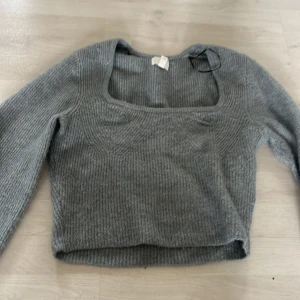 Grå ribbad stickad tröja - Säljer en stilren grå stickad tröja med ribbad struktur och fyrkantig halsringning. Tröjan har långa ärmar och en bekväm passform, perfekt för kyligare dagar. Passar bra till både jeans och kjol.