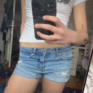 Blå jeansshorts - Säljer ett par blå jeansshorts med slitna detaljer och upprullade benslut. Perfekta lågmidjade för sommardagar och en avslappnad stil. De har en klassisk femficksdesign och knappgylf. Storlek är 150 men passar bra för 150-160 också! Jag är 160 och känner att de börjar bli lite små på mig💕