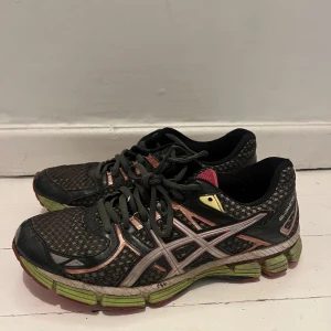 Svarta och rosa löparskor från Asics - Säljer ett par svarta löparskor från Asics med rosa och gula detaljer. Skorna har snörning och en mönstrad ovandel i syntetmaterial. Sulan är grön och rosa med bra dämpning för löpning.
